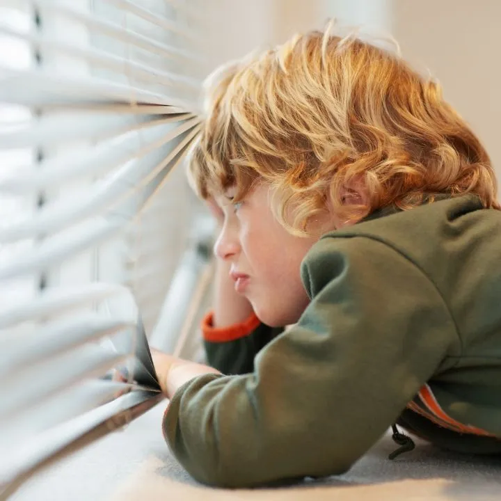 Child looking out a window blind as a watchful neighbor