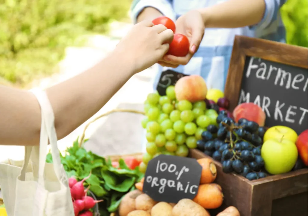 Close up of woman handing over tomatoes to a vendor at a fruit stand
