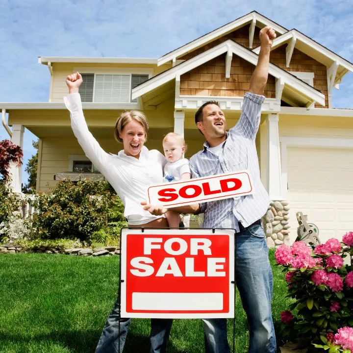 Happy buyers celebrating with a sold sign in front of their home