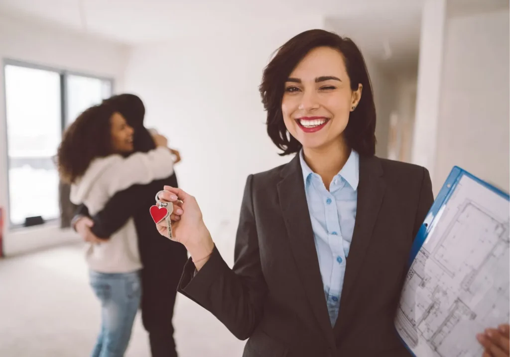 Happy Couple embracing in the background while real estate agent holds their new home keys.