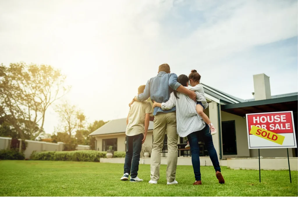 Happy family looking at their new home with a Sold sign on it