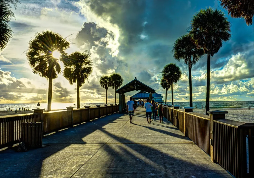 People walking on a waterfront boardwalk with palm trees