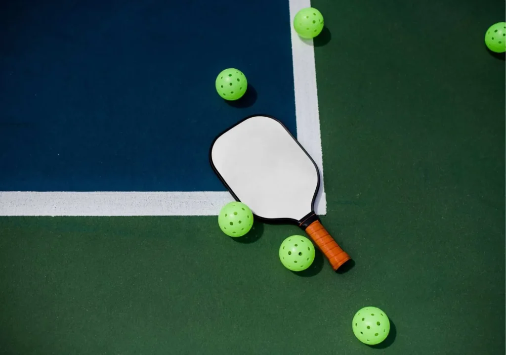 Pickleball paddle with 5 balls laying on a green court