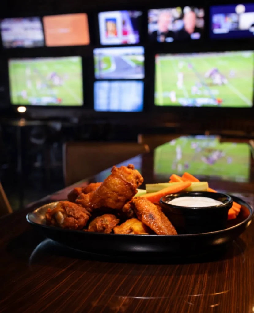 Plate of chicken wings in front of TV screens at The Tipsy Corner