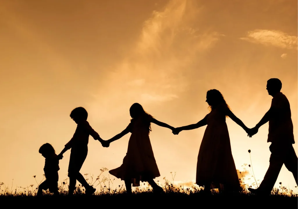 Silhouetted in black, a family holding hands walking at sunset