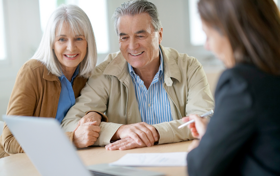 Smiling older couple meeting with a real estate agent at a laptop