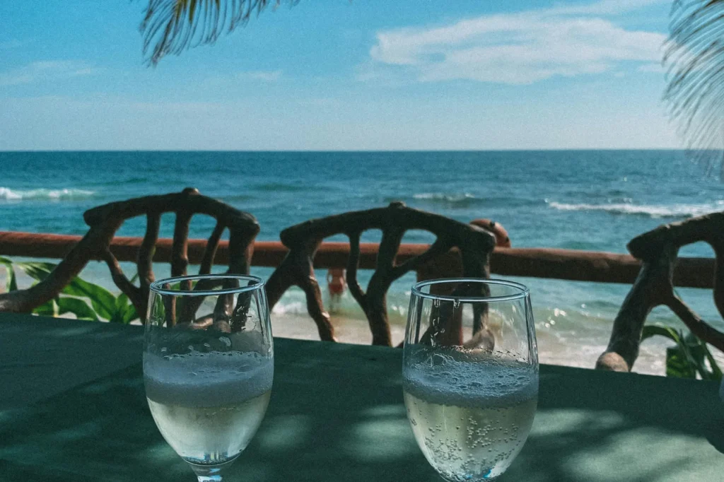 Two wine glasses on a table overlooking the beach