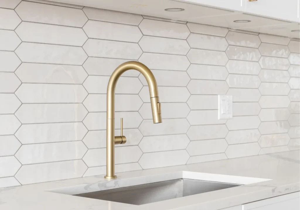 White tile backsplash behind a gold tone kitchen faucet
