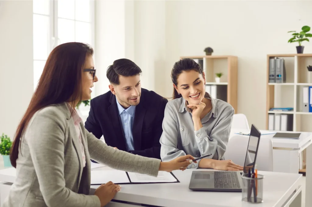 Woman real estate agent reviewing information with couple on her laptop