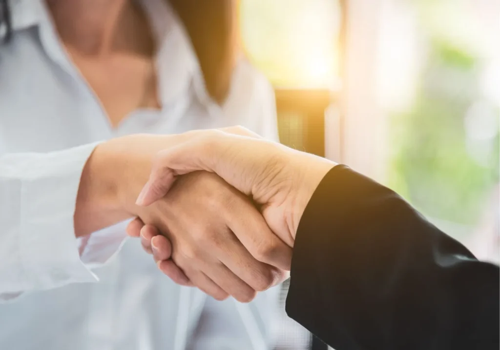 Woman with white blouse shaking hands with someone with a black jacket sleeve